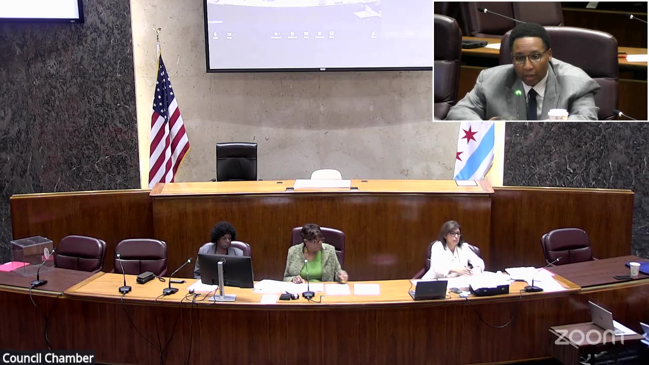 Ald. Jason C. Ervin (28th Ward), shown in an inset, speaks for Harvest Homes II at the Committee on Finance as members sit at the dais, Oct. 13, 2026